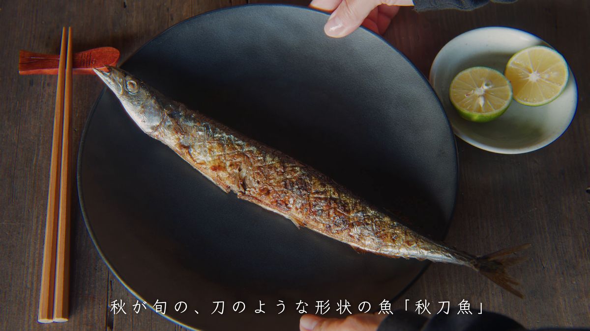 黒い皿の焼きサンマと半分に切ったすだち