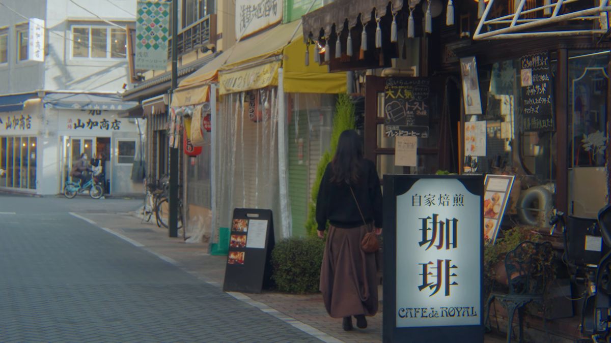 喫茶店の看板の前を通る後ろ姿