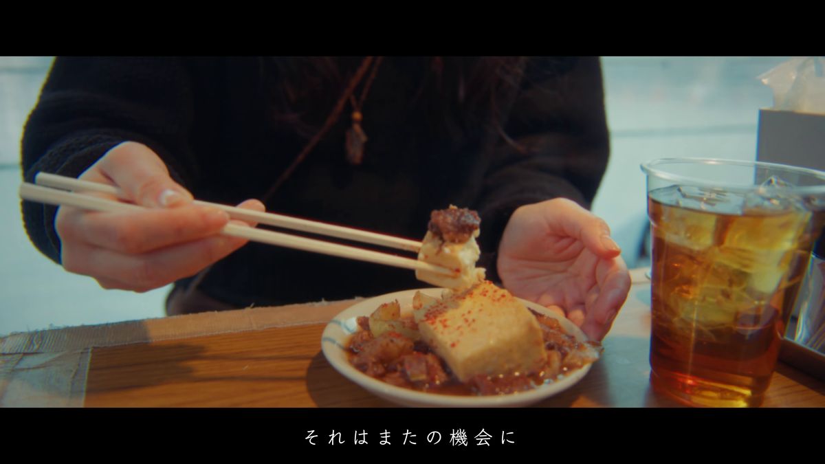 煮込みを箸でつまむ、冷たい飲み物を添えて