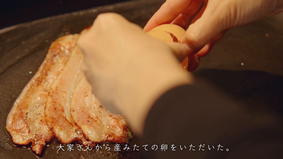 ベーコンの上に卵を割り入れる手元