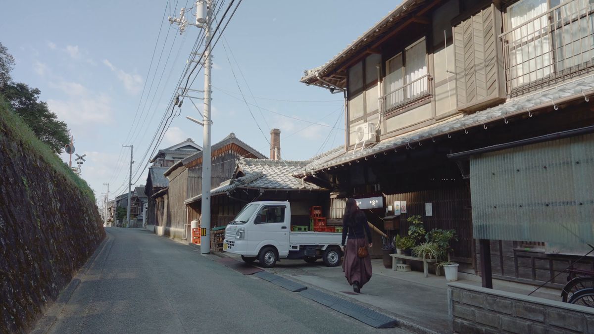 古い町並みの路地を歩く後ろ姿と軽トラック