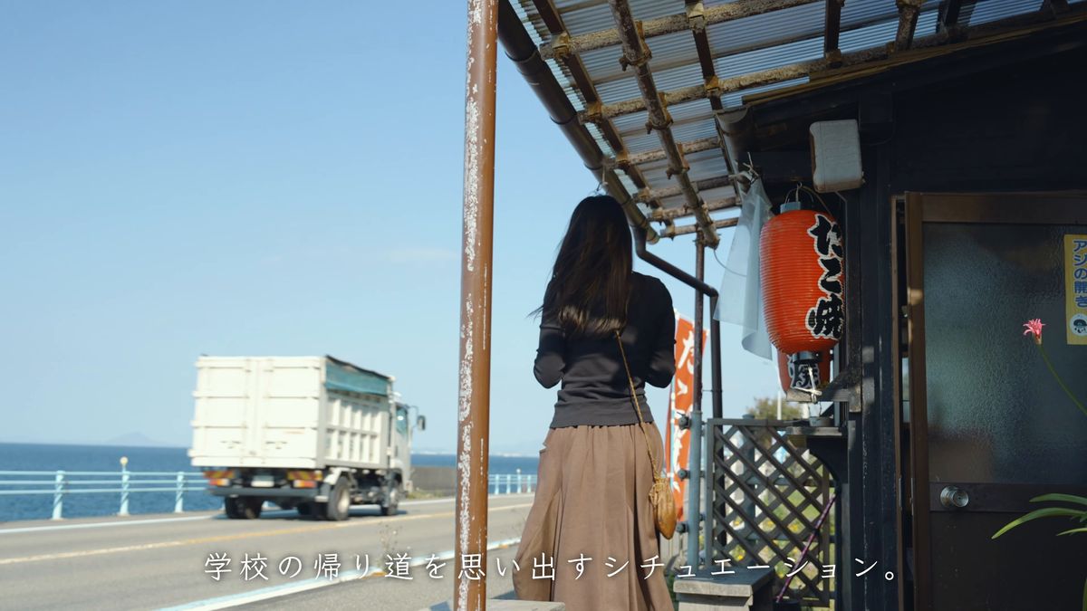 店先で待つ後ろ姿と、通り過ぎるトラック