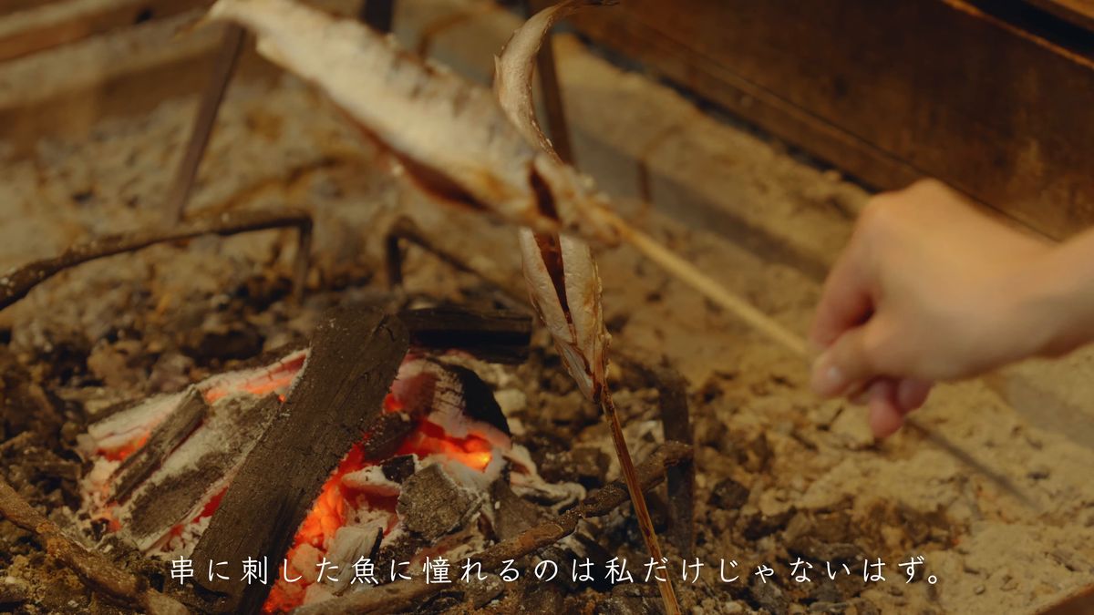 炭火のそばで焼ける串刺しの魚