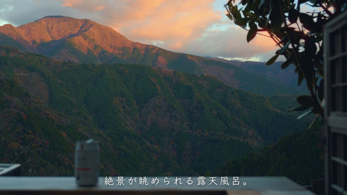 湯船の縁の缶ビールと夕日に染まる山