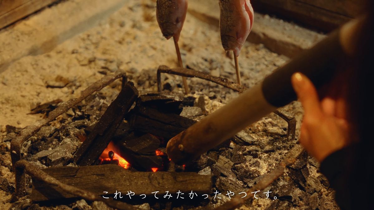 火箸で炭を寄せる手元と、灰に立てた串