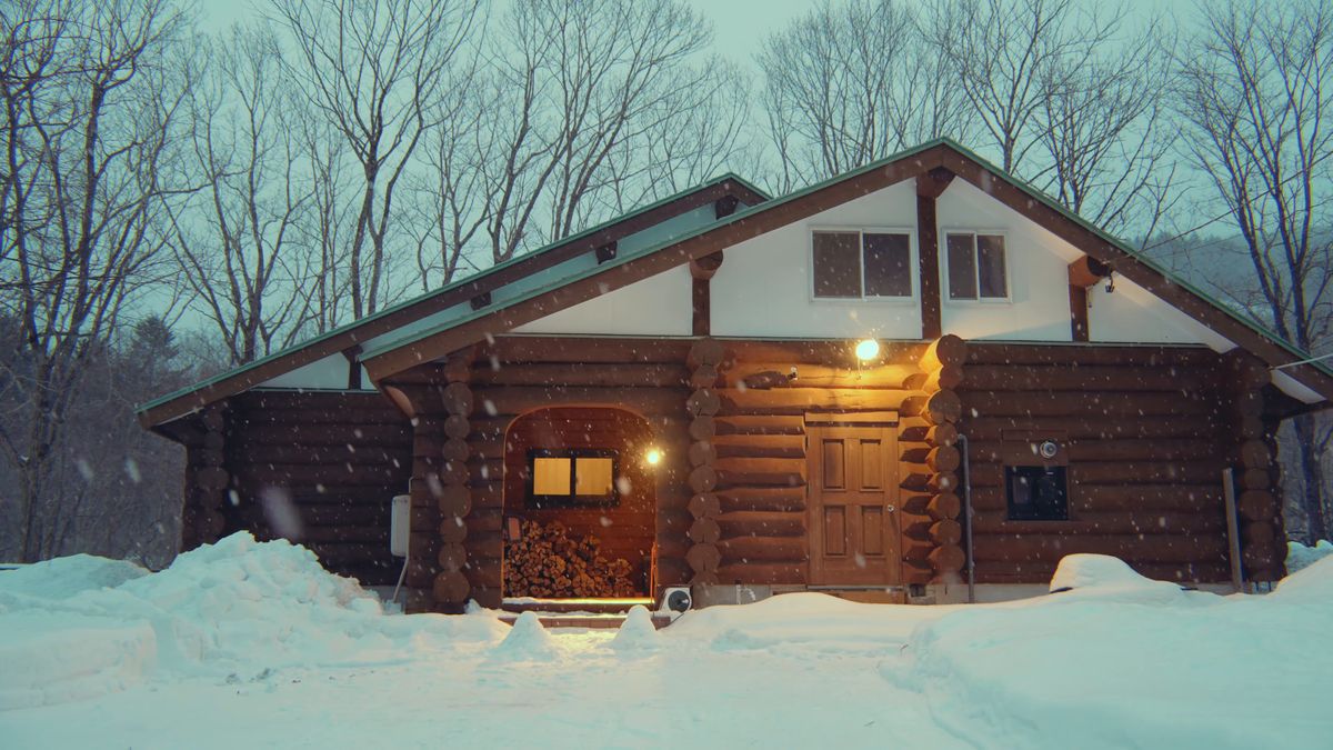 夕暮れ、雪の中で灯りのともったログハウス