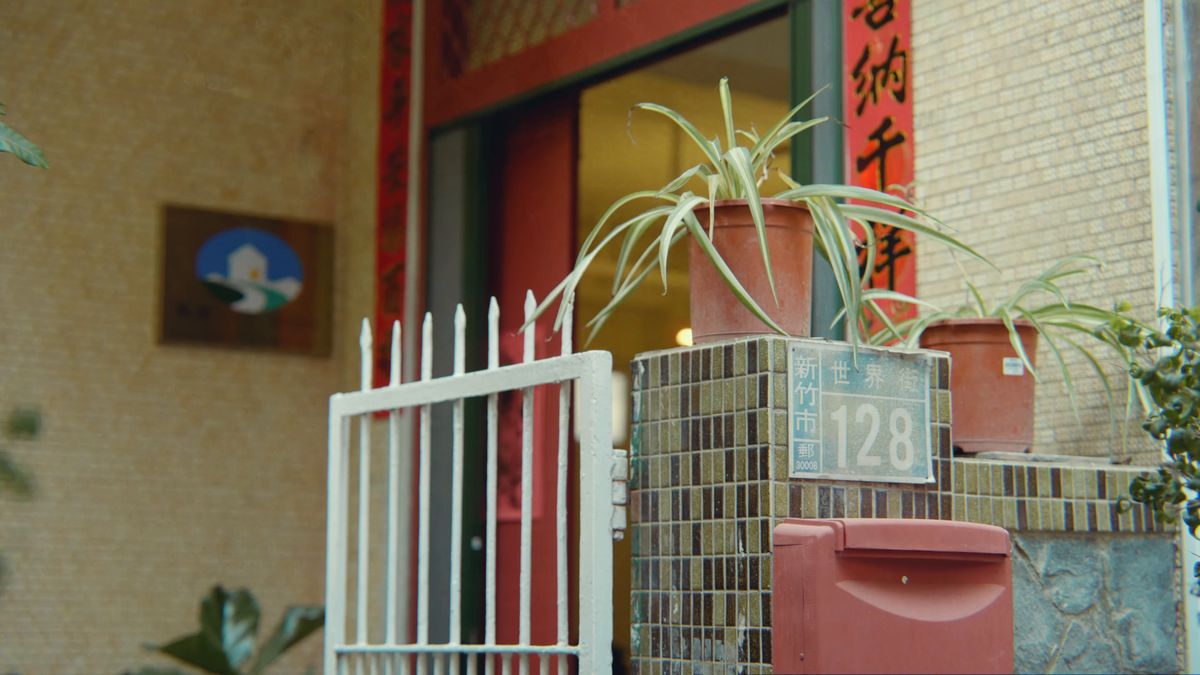 白い柵の門と赤い郵便受け、鉢植えの緑