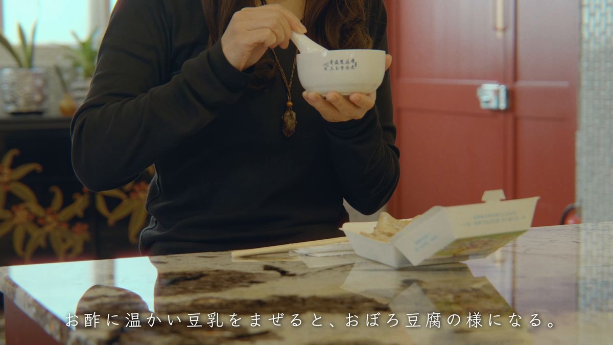 赤い扉の前で鹹豆漿の器を手にする