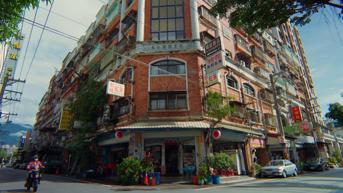 赤レンガの角の建物と、通りを走るスクーター