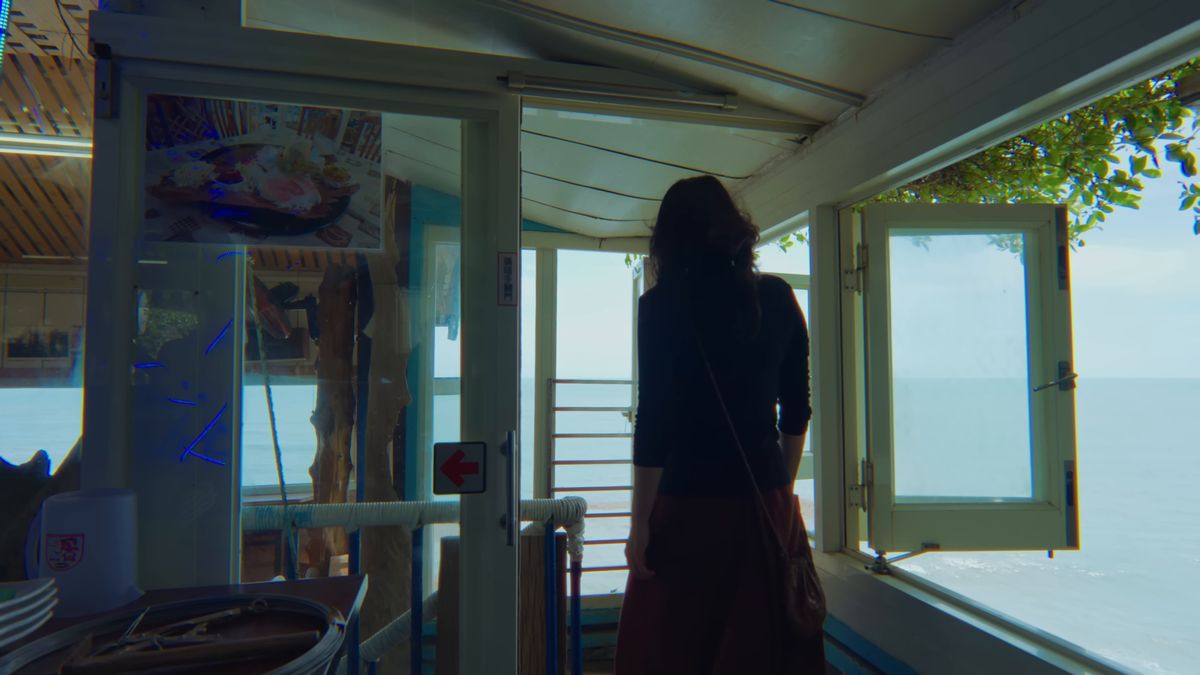 海に向かって窓の開いた店の入口に立つ後ろ姿