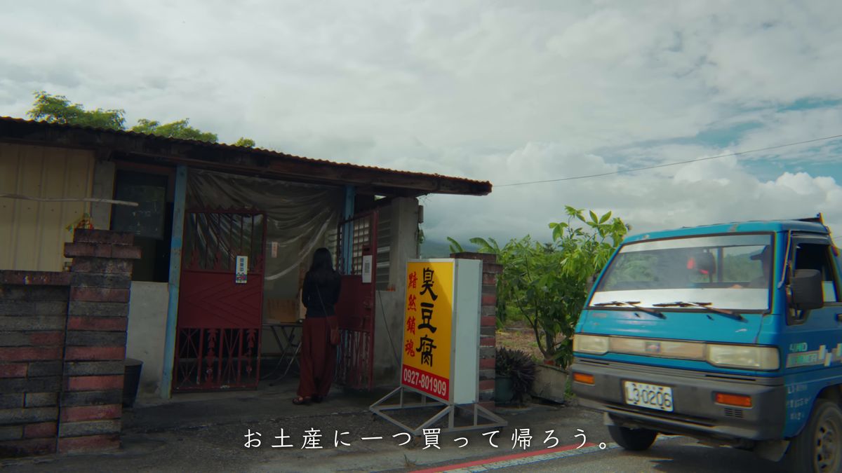 臭豆腐の店先に立つ後ろ姿と、走ってくる青いトラック