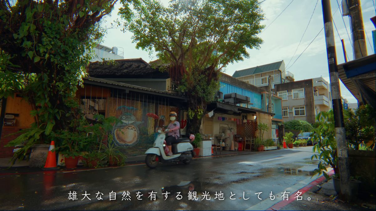 雨上がりの通りを走るスクーターと壁画