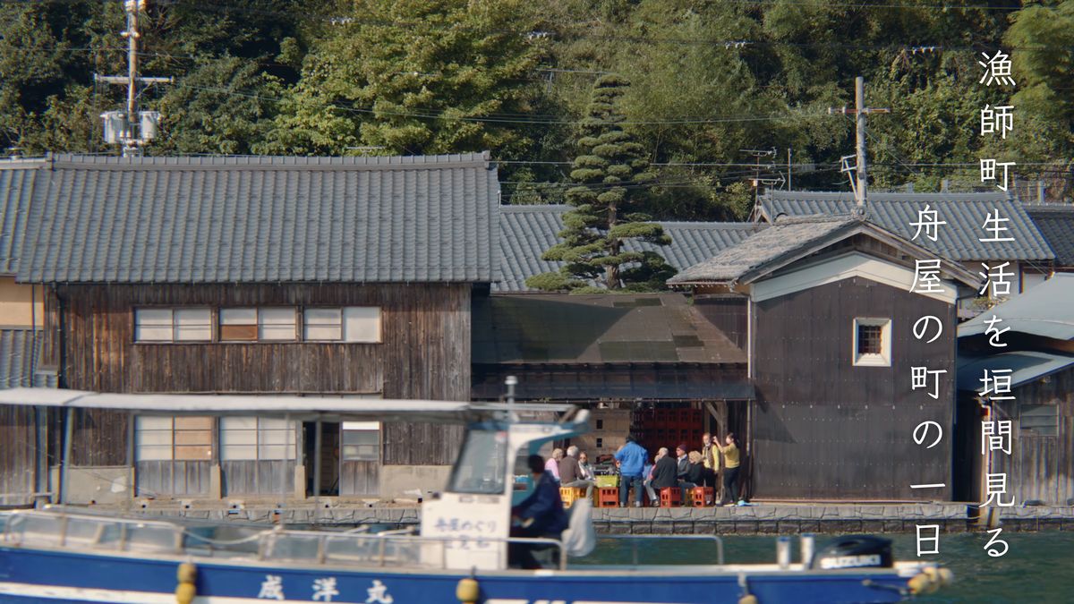 舟屋の前を通る遊覧船と、岸辺に座る人たち