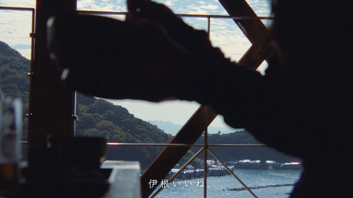 逆光のシルエットで丼を持ち上げる、向こうに湾