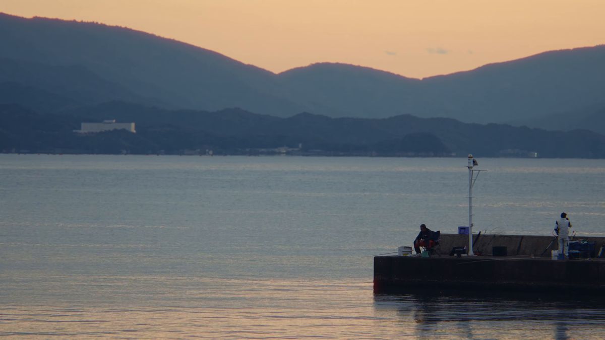夕暮れの海と、防波堤の先で釣りをする人影