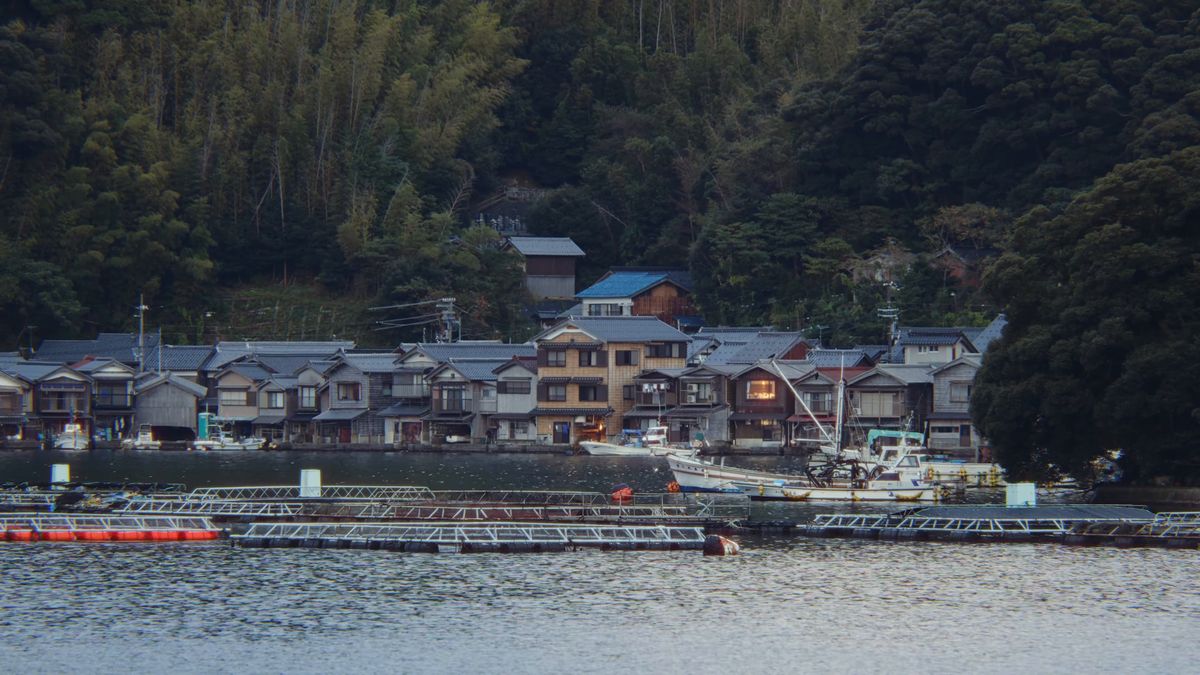 夕暮れの色に沈む舟屋の並びと、手前のいけす
