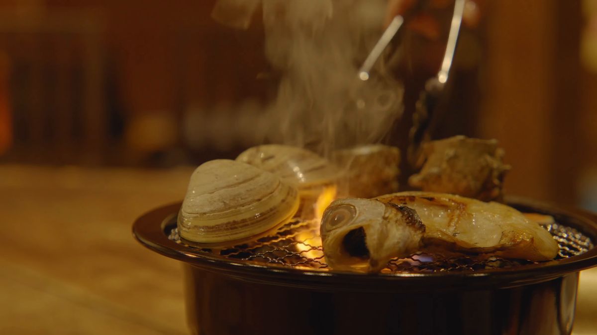 煙の立つ網の上の貝と魚をトングで返す