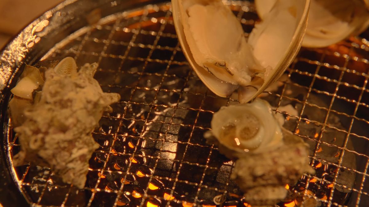 炭火の網の上のサザエと、殻の開いたハマグリ