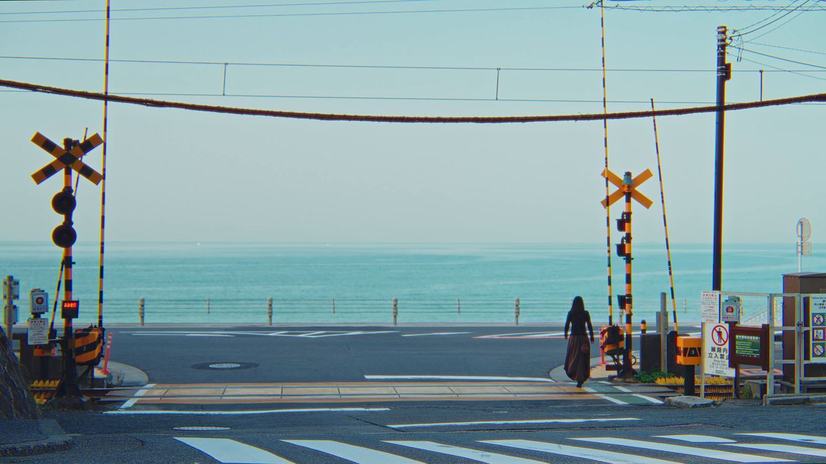 踏切の向こうに海が広がる道を歩く後ろ姿