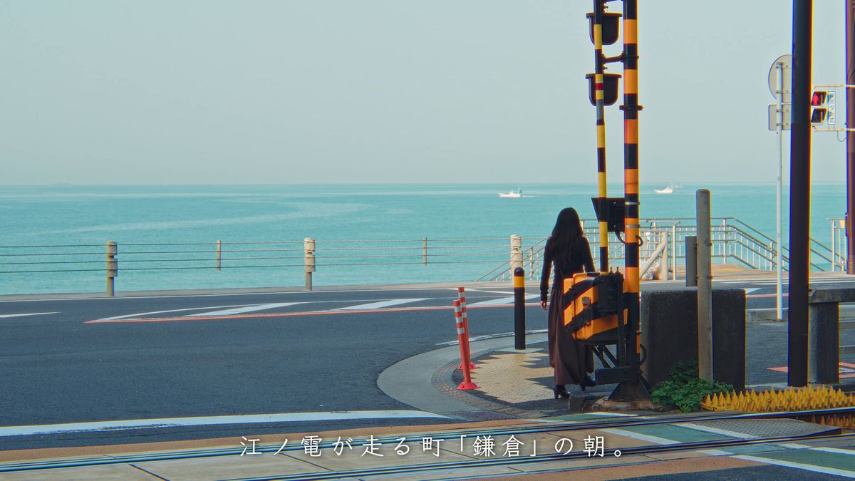 黄色と黒の踏切の柱と、海沿いの道