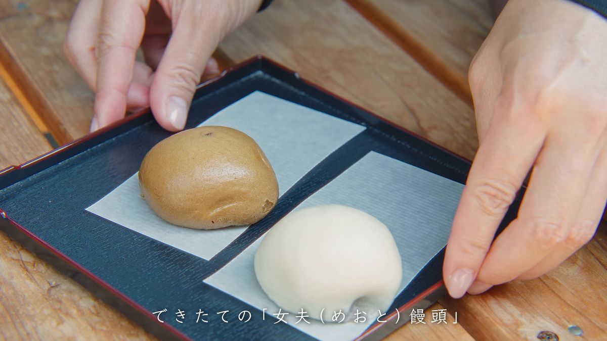 黒い盆に茶と白の饅頭を置く手元
