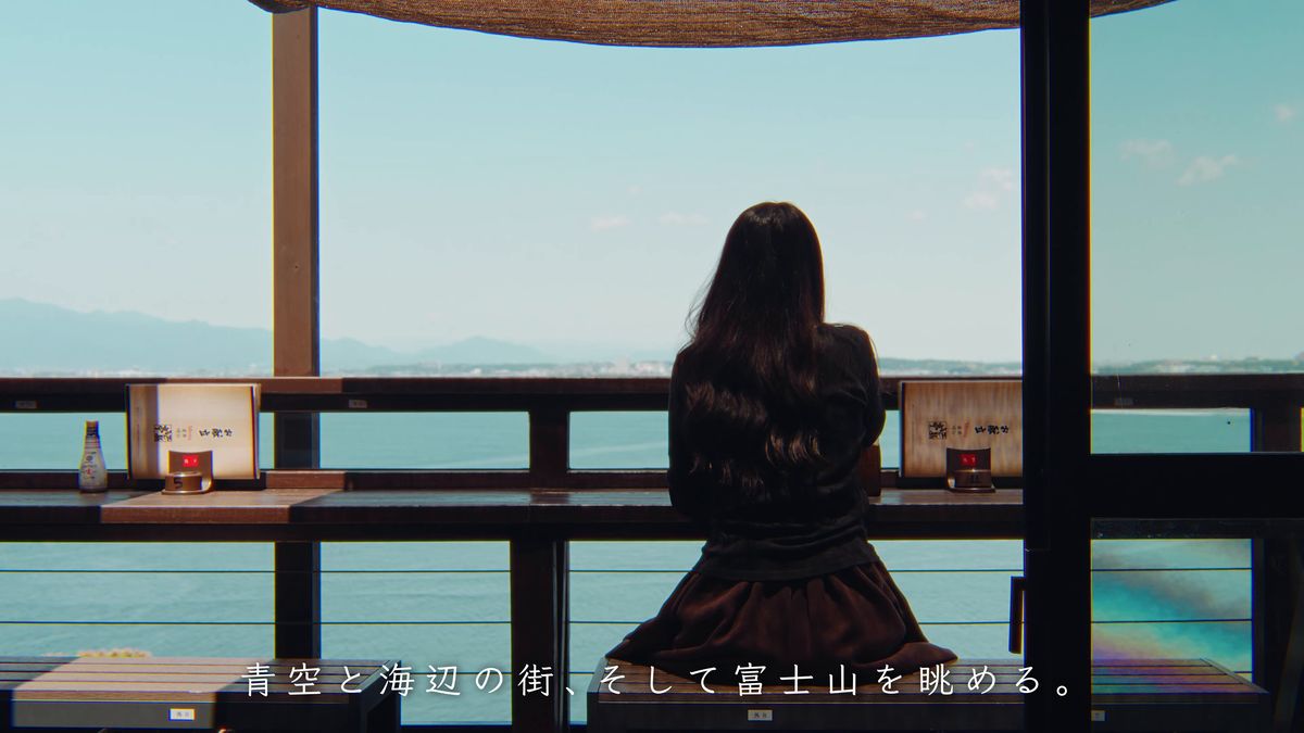 窓辺の席に座り海を眺める後ろ姿
