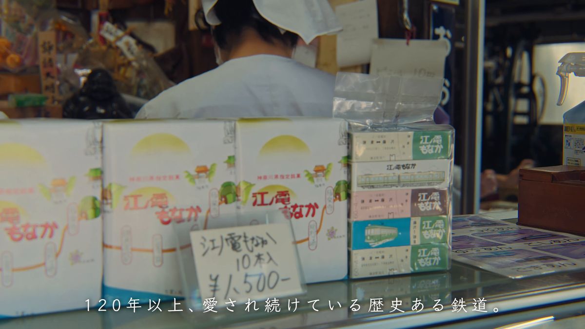 江ノ電の絵の箱が並ぶカウンターと、包む店の人の後ろ姿