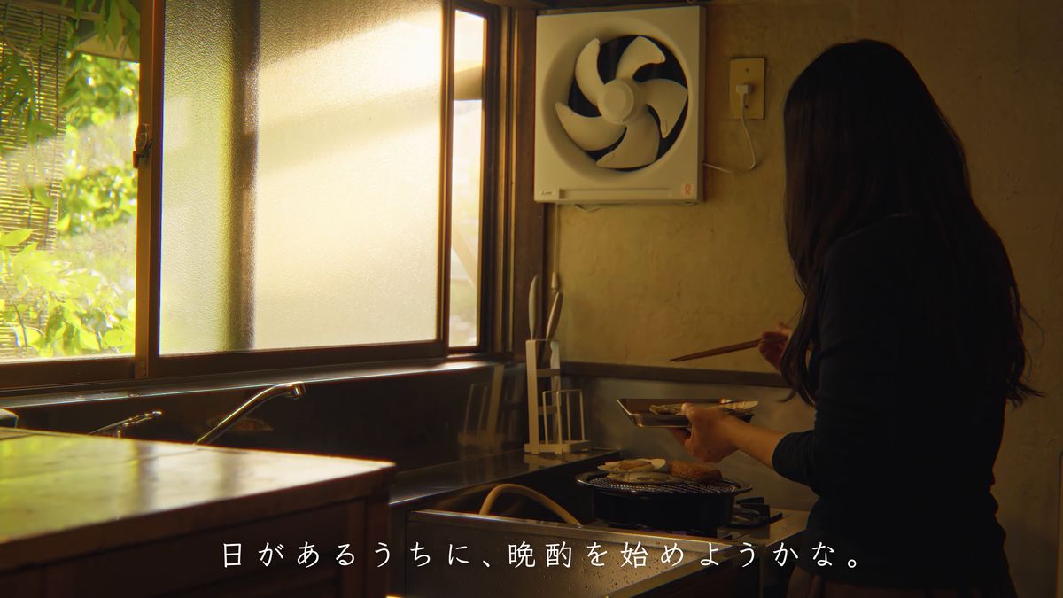 窓の光が差す台所で支度をする後ろ姿