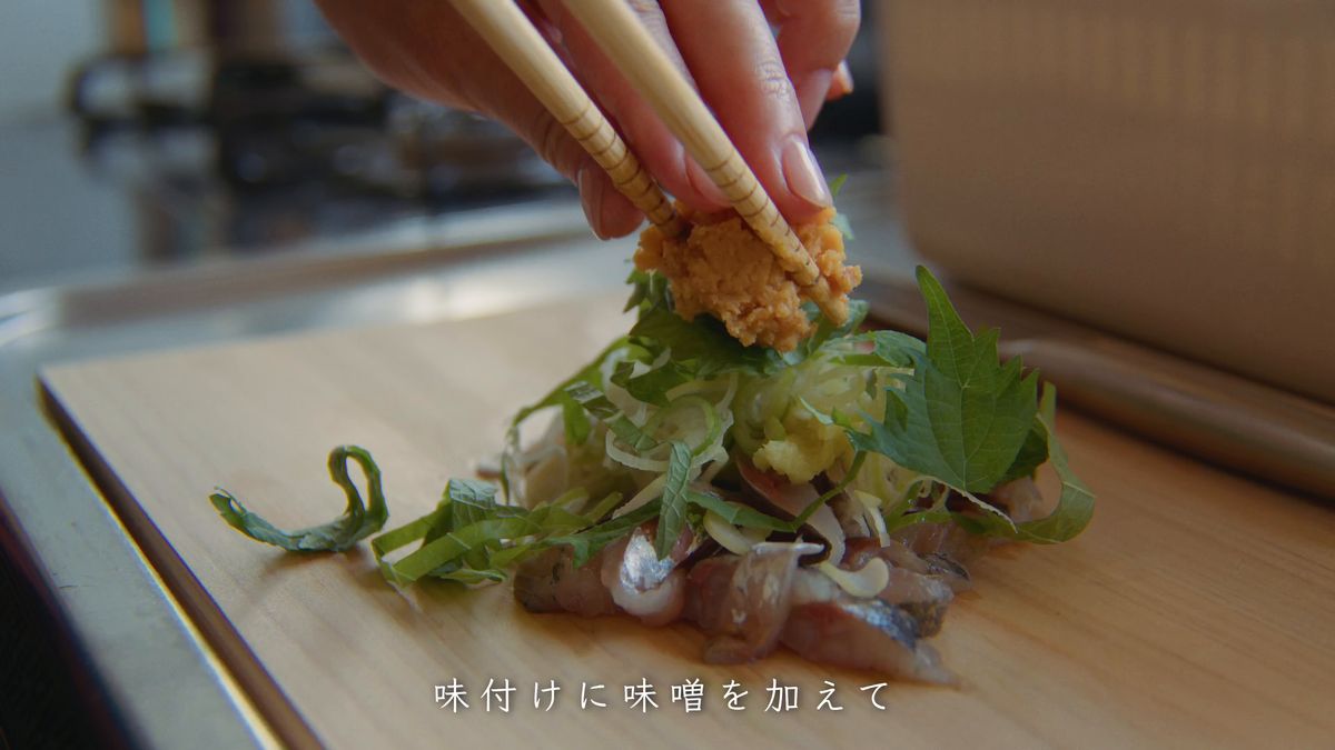 薬味をのせたアジに箸で味噌を加える
