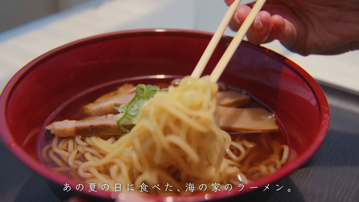 赤い丼の醤油ラーメンを箸で持ち上げる