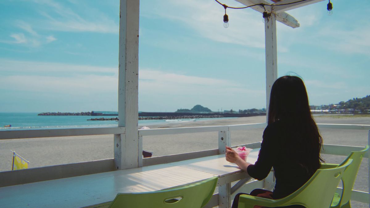 海の家の席から砂浜と海を眺める後ろ姿