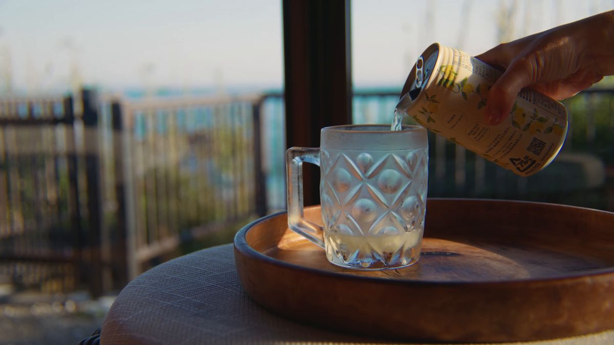 窓辺でグラスに缶の飲み物を注ぐ