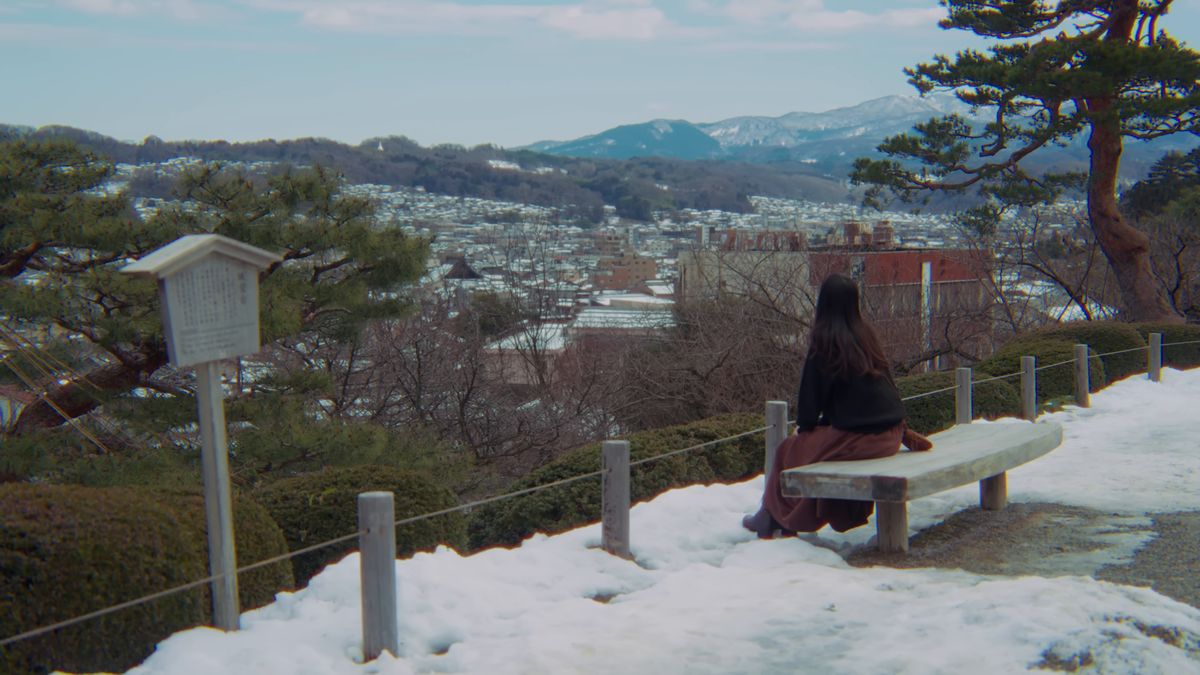 雪のベンチに座り、金沢の町と山を眺める