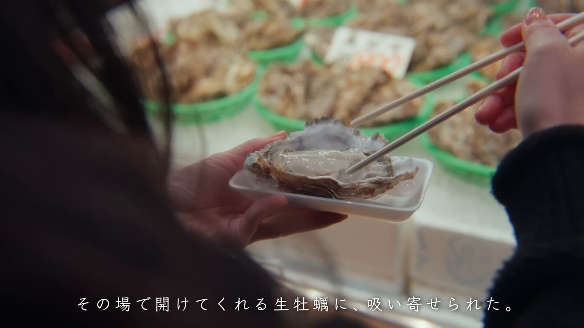 店先で牡蠣を箸でつまむ
