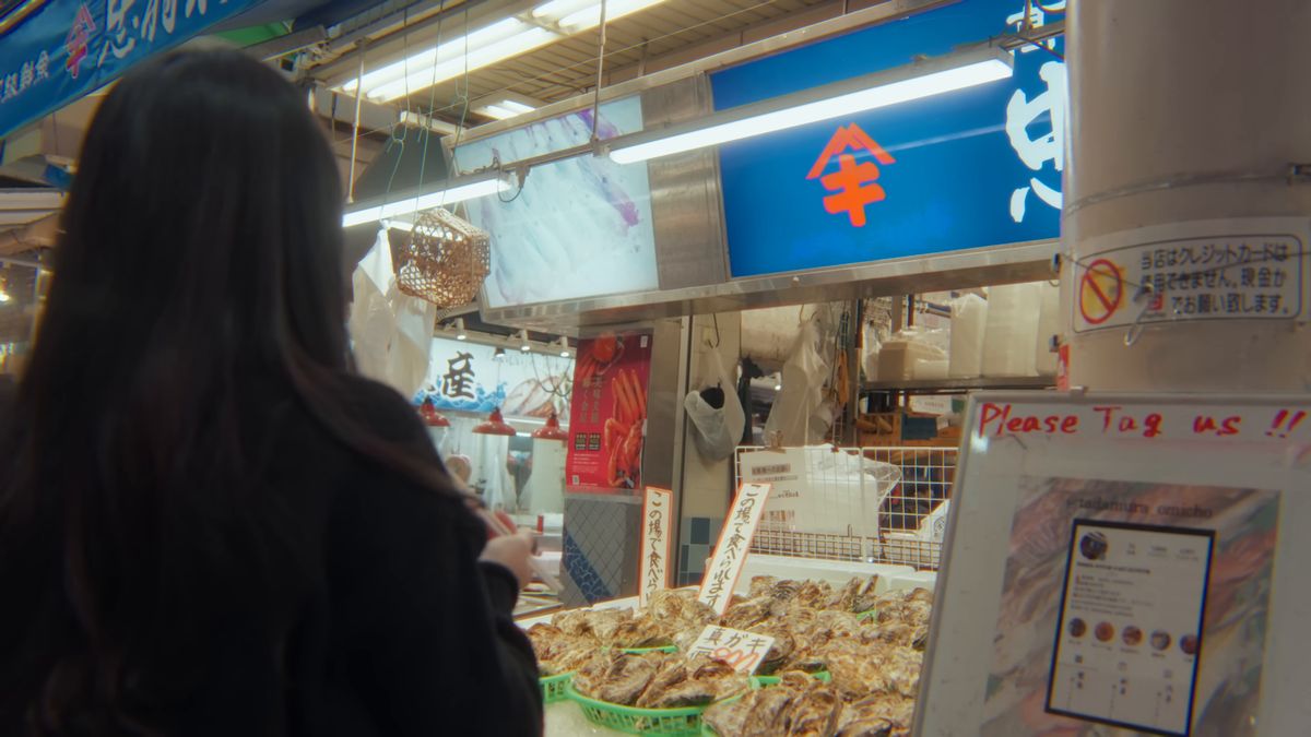 牡蠣の籠が並ぶ鮮魚店の前に立つ後ろ姿