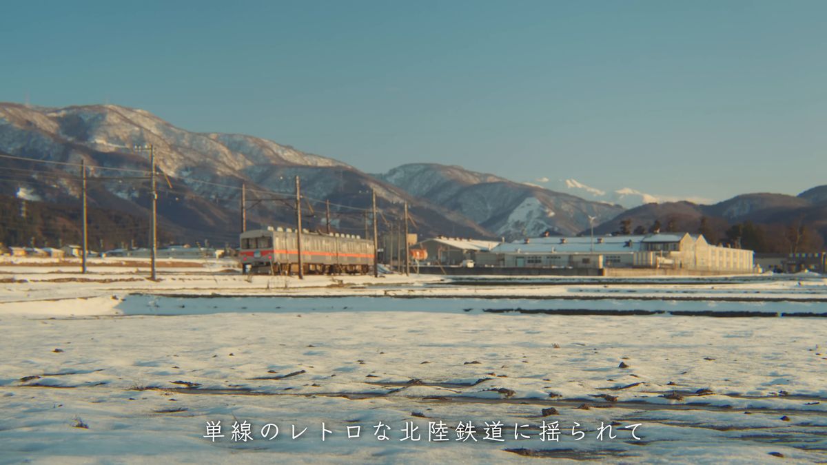 雪の田んぼの向こうを走る電車と山並み
