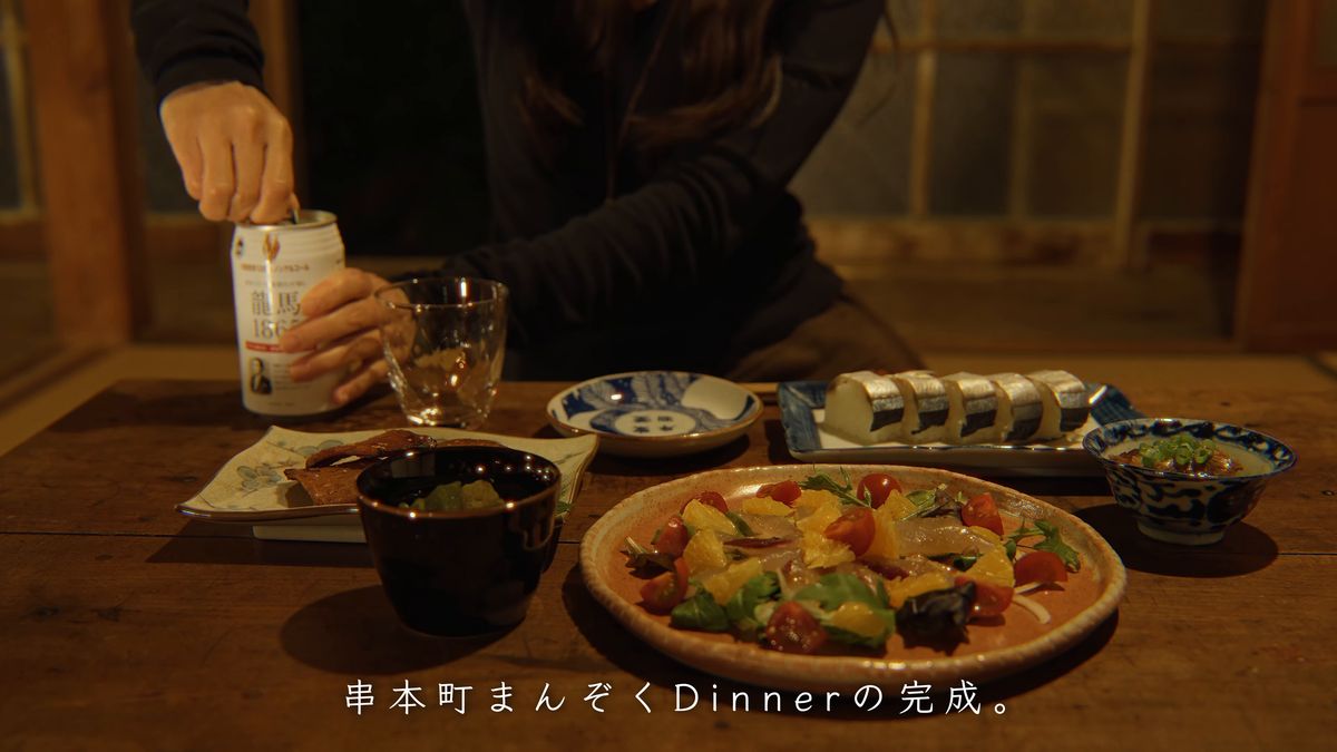 カルパッチョとさんま寿司の並ぶ食卓に缶を置く手元