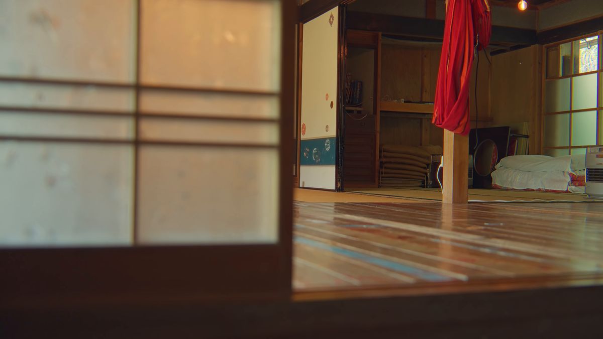 梁から赤い布が下がる板の間と畳んだ布団