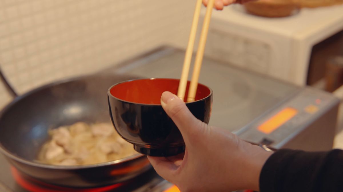 黒い椀で卵を溶く箸と、鶏肉を煮る鍋