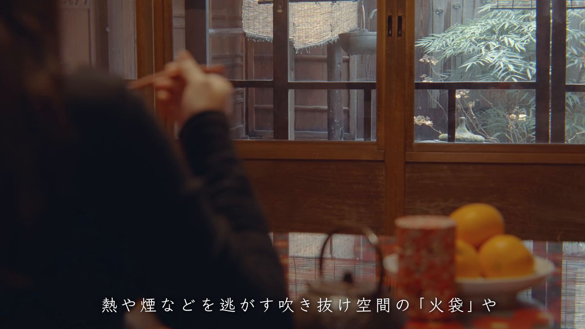窓辺の食卓に向かう後ろ姿と、鉄瓶とみかん