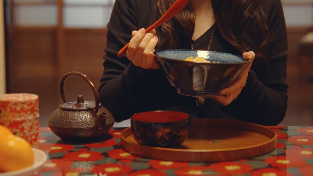 赤い花柄の卓で、丼を手に食べる