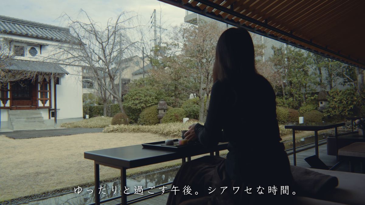 庭を眺めて座る後ろ姿と、庭の奥の白い蔵