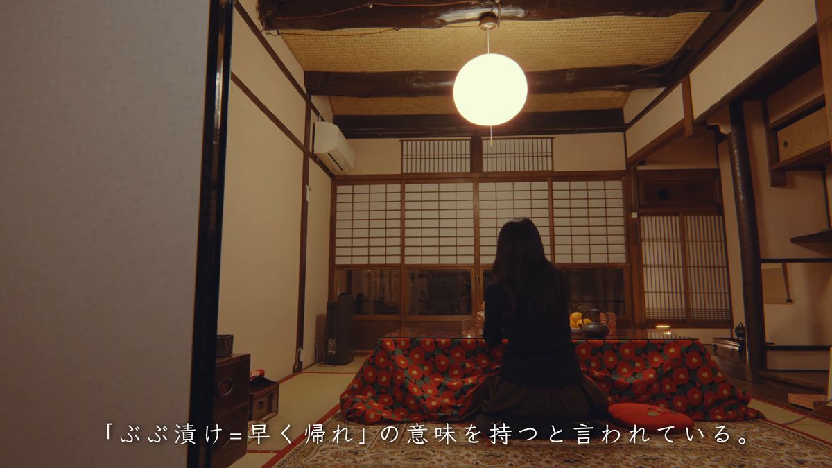 丸い照明の下、赤い花柄の座布団に座る後ろ姿