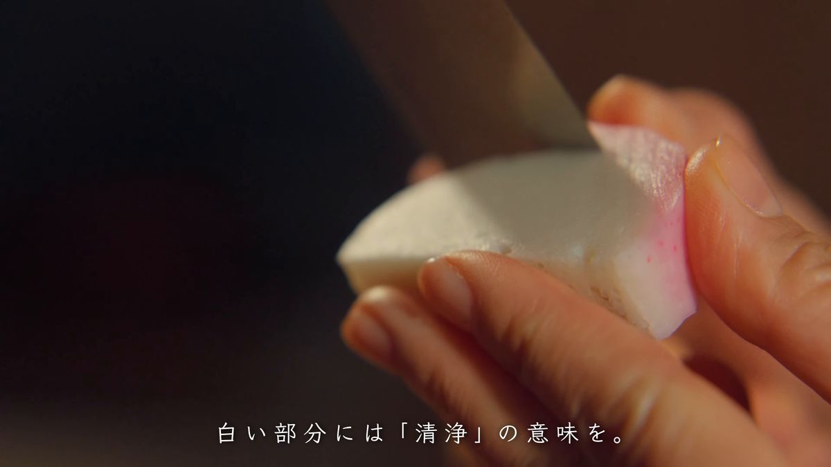 白いかまぼこの赤い皮に包丁を入れる