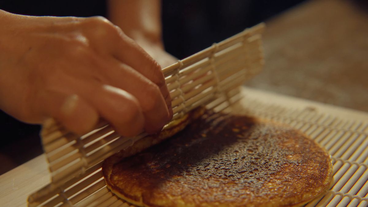 焼き色の付いた伊達巻を、巻きすで巻きはじめる