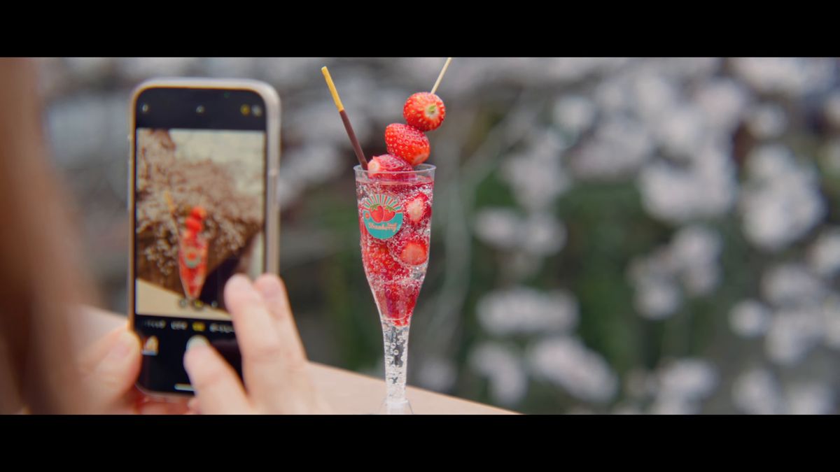 桜を背に、苺の飲み物をスマートフォンで撮る