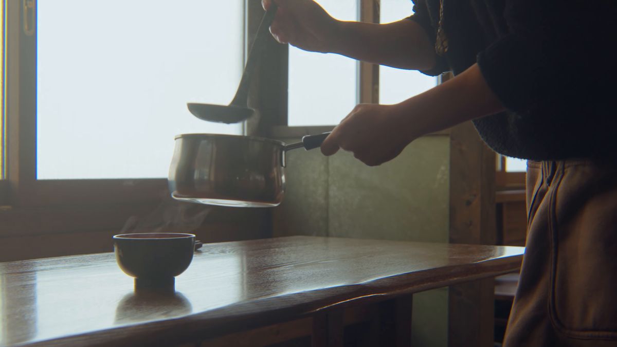 窓辺で、鍋から椀に汁を注ぐ
