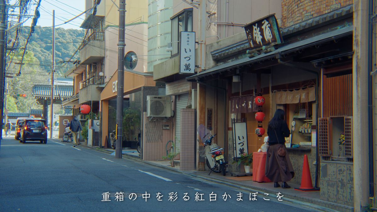 「いづ萬」の看板が出た通りと、店先に立つ後ろ姿