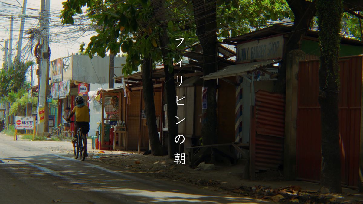 木陰の道を走る自転車と、道沿いの小さな店