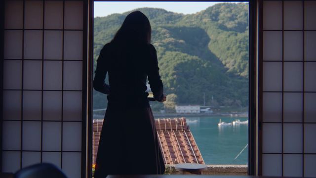 障子の窓辺に立ち、瓦屋根越しの湾を眺める後ろ姿